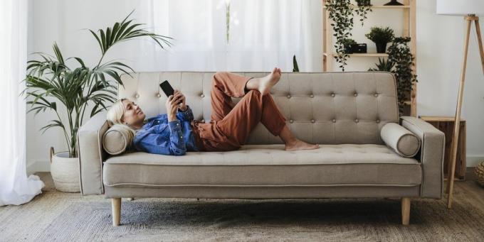 אישה צעירה משתמשת בטלפון נייד שוכבת על הספה בבית