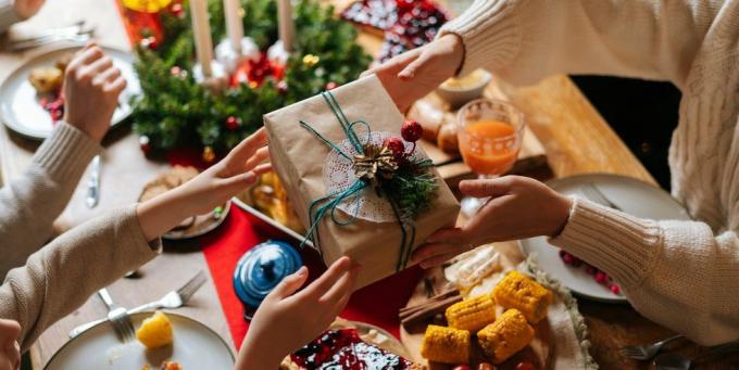 מקרוב מבט מלמעלה של הורה אוהב בלתי מזוהה נותן קופסה חגיגית עם מתנת חג המולד לבן המאושר יושב ליד שולחן סעודה